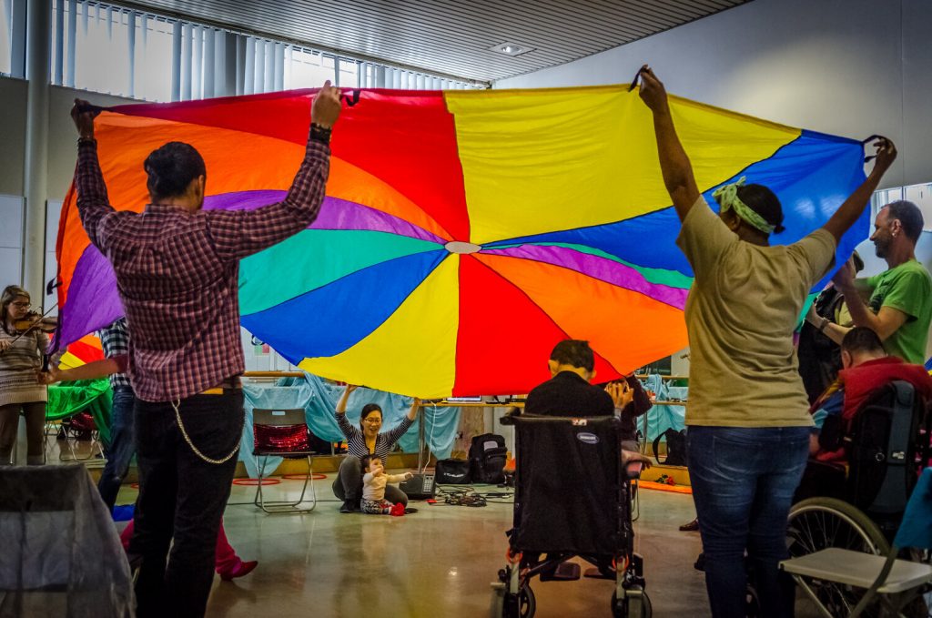 People raise a multicoloured parachute over the heads of other people